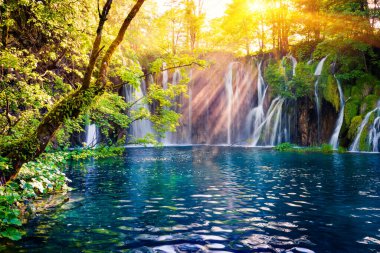Son güneş ışığı Plitvice Ulusal Parkı 'ndaki saf su şelalesini aydınlatıyor. Mavi göllü yeşil ormanın renkli bahar manzarası. Hırvatistan ve Avrupa 'nın kırsal manzarası harika. Doğa konseptinin güzelliği.