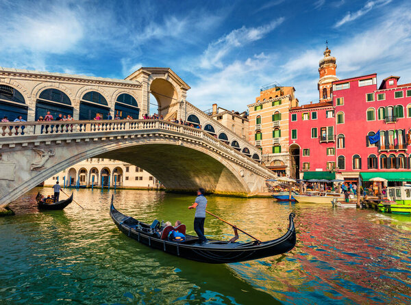 Colorful morning view of Rialto Bridge. Amazing cityscape of  Venice with tourists on gondolas, Italy, Europe. Romantic summer scene of famous Canal Grande. Traveling concept background.