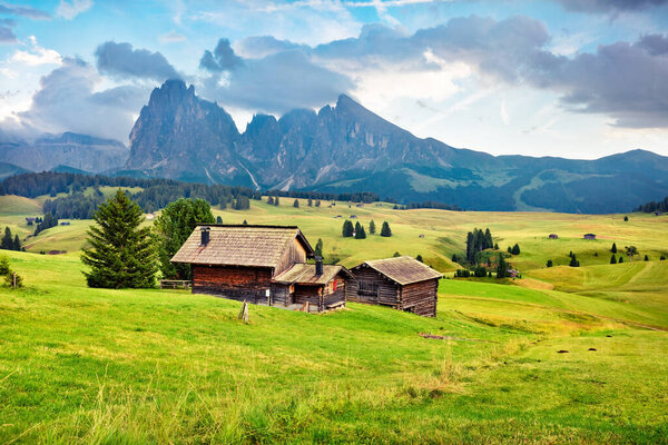 Colorful morning scene of Compaccio village with Sassolungo / Langkofel peak on background, Seiser Alm or Alpe di Siusi location, Bolzano province, Italy, Europe. Colorful summer sunrise of Dolomiti Alps. 