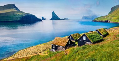 Arka planda tipik çimenlik evler ve Tindholmur kayalıkları olan Bour köyünün güneşli yaz manzarası. Vagar Adası, Faroe, Danimarka, Avrupa 'nın panoramik sabah manzarası. Seyahat konsepti arka planı