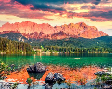 Zugspitze sıradağlarıyla Eibsee gölünde renkli bir yaz günbatımı. Alman Alpleri, Bavyera, Garmisch-Partenkirchen köyü, Almanya, Avrupa 'da muhteşem bir açık hava sahnesi. İşlenmiş fotoğraf sonrası sanatsal stil.