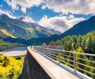 Fotoğrafçı, Orlegna nehrindeki barajda fotoğraf çekiyor. Maloja geçidinin tepesinden güneşli yaz manzarası. İsviçre Alpleri, Grisons, İsviçre, Avrupa kantonunda Upper Engadine. İşlenmiş fotoğraf sonrası sanatsal stil.