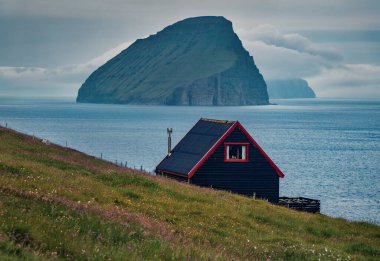 Tipik Faroe kara duvarlı evi ve arka planda Koltur adası. Sandavagur Köyü, Vagar Adası, Faroe, Danimarka, Avrupa 'nın kasvetli yaz manzarası. 