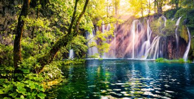 Son güneş ışığı Plitvice Ulusal Parkı 'ndaki saf su şelalesini aydınlatıyor. Mavi gölü olan yeşil ormanın renkli bahar manzarası. Hırvatistan ve Avrupa 'nın kırsal manzarası harika. Orton Efekti