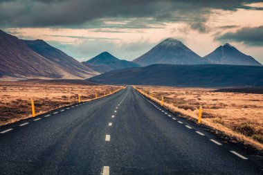 Dramatik bulutlu gökyüzü ile boş asfalt yol. Volkanik tepeleri olan tipik İzlanda manzarası. Seyahat kavramı arkaplanı resmi.