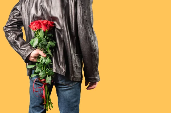 Man with a bouquet of red roses behind his back. Elegant man holding red rose flowers in hand. Romantic and valentines day holiday concept