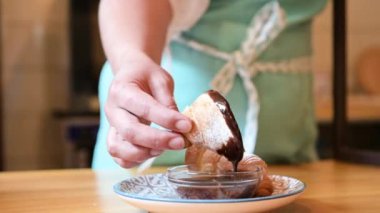Bir kadının eli sıcak çikolataya kruvasan döküyor. Kruvasan üzerine siyah çikolata.