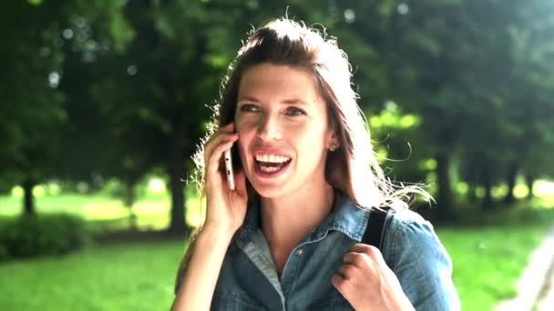 若い女性が夏の公園で電話で話している 太陽の公園で携帯電話を持つ少女は ボケの肖像画を閉じます 夏の自然景観 週末のレクリエーション ビジネスの女性は電話を使う スローモーション — ストック動画