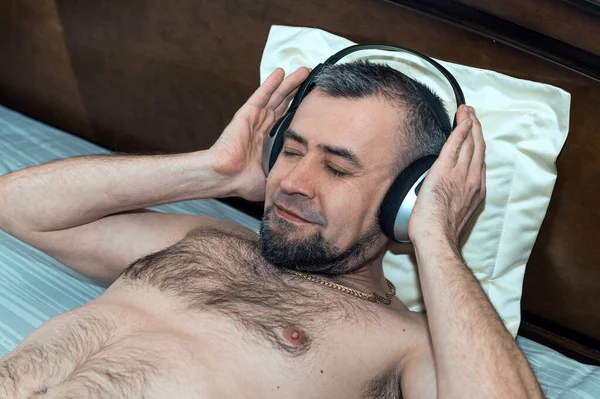 Man listening to music on headphones at home while lying on bed. Cheerful man listening music with wireless headphones