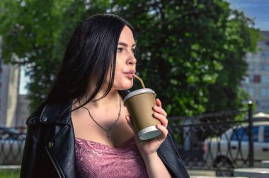 Sokakta kahve içen genç bir kadın. Şehir caddesinde sıcak bir içecek içen bir kadın. Teras kafeteryasında kahve içen çekici genç bir kadın resmi