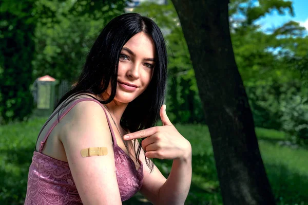 Smiling female with band-aid on arm after vaccination.. Woman feeling positive after getting vaccinae. Happy teenage girl outdoor