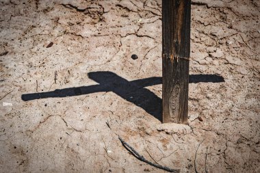 Eski yıpranmış bir haç çatlamış ama kırılmamış ve gölgesi Fabens, Teksas 'ın güneyindeki La Isla Mezarlığı' nın sıcak çöl kumunda duruyor..