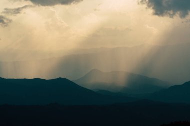 Dağın tepesi bulutlarla, yağmurla ve güneşle örtüşüyor..