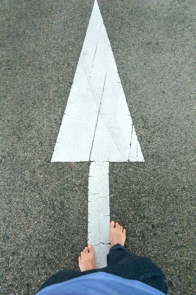 man\'s foot on jogging pant on asphalt road with white arrow