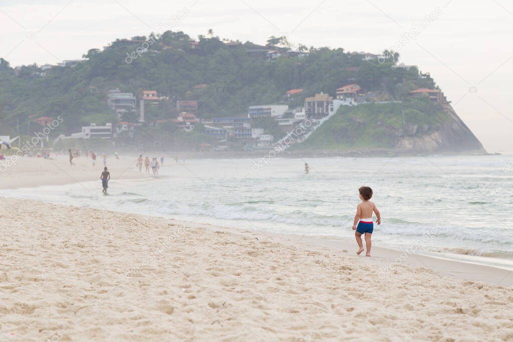 Little boy of his backs walking on the beach. Barra da Tijuca, Rio de Janeiro, Brazil.