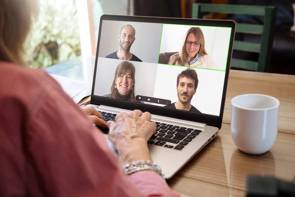 Bir grup genç kızla video görüşmesiyle konuşan yaşlı bir kadının omzunun üstünden bak. Gülümseyen insanlarla dolu dizüstü bilgisayar ekranı. 60 'lı yaşlarda yaşlı bir büyükanne oğullarıyla sanal sohbetin keyfini çıkarıyor. Yeni teknoloji kullanımı kavramı