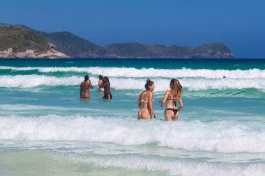 CABO FRIO, RIO DE JANEIRO, BRAZİL - 26 Aralık 2019: iki güzel kız deniz dalgalarının ortasında eğleniyor. Suda yıkanan insanlar..