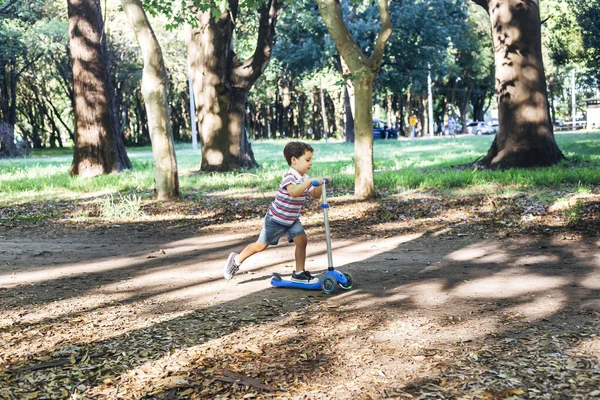 Parkta scooter kullanan bir çocuk. Çocuklar paten kaymayı öğreniyor. Küçük çocuk güneşli yaz gününde paten kayıyor. Güvenli sokaktaki çocuklar için açık hava aktivitesi. Anaokulu çocuğu için aktif spor.