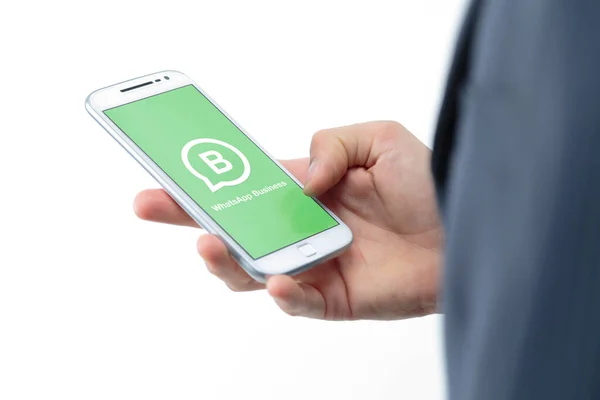 ROSARIO, ARGENTINA - JANUARY 30, 2021: WhatsApp business application on the screen of a smartphone. Young businessman with a white cell phone in hand. Software for communication over the internet.