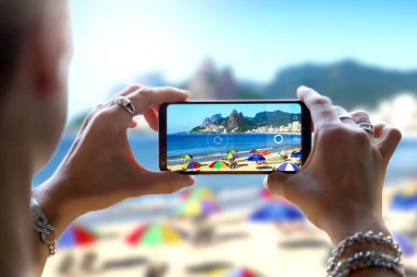 Ipanema Plajı 'nda cep telefonuyla fotoğraf çeken bir kadın. Brezilya, Rio de Janeiro 'da bir akıllı telefon kamerasıyla fotoğraf çekmek..
