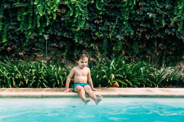 Küçük çocuk yüzme havuzunun sınırında oturuyor..