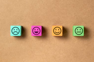 Emoticon faces in colors wooden blocks over brown paper. Service evaluation and satisfaction survey concepts. Angry, neutral, good mood and happy. Copy space. clipart