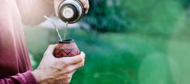 Sıcak suyla eş hazırlayan bir adam. Kabak çiftinin içinde yerba var. Orta yaşlı Latin Amerikalı adam gün batımının tadını çıkarıyor. Kopyalama alanı olan sancak biçimi.
