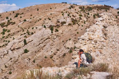 Sırt çantalı yaşlı Asya 'lı erkek turist yazın bir dağ yamacının arka planında fotoğraf çekiyor..