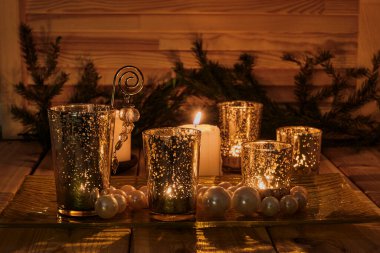 Pencere kenarında yeni yıl ya da Noel akşamı kompozisyonu. Yanan mumlar, altın cam şamdanlar, küçük toplar, ahşap arka planda köknar dalları.