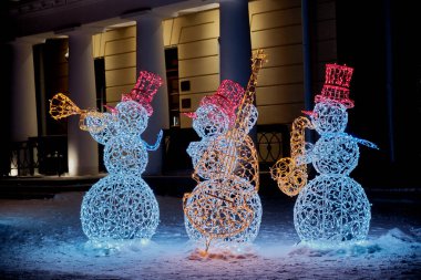 Yekaterinburg, Rusya - 4 Ocak 2021: Tel ve çelenklerden yapılmış üç renkli parlak kardan adam bir kış gecesi sokak ortasında caz çalıyorlar.