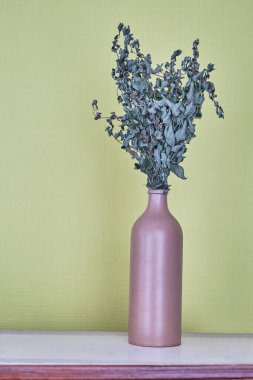 Sarı-yeşil bir duvarın arka planına karşı kilden bir vazoda kurumuş nane filizleri. Durgun hayat.