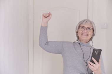 Gri saçlı, gözlüklü, kulaklıklı, gri boğazlı, evde cep telefonuyla konuşan ve hayal kırıklığı yaşayan son sınıf öğrencisi bir kadın. İnsanlar iletişim kurar. Yaşam tarzı anı.