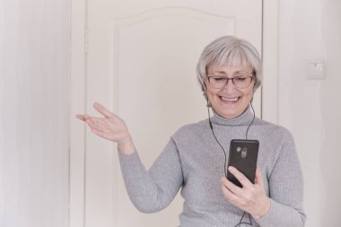 Gri saçlı, gözlüklü, boğazlı ve cep telefonuyla konuşan son sınıf öğrencisi bir kadın. İnsanlar iletişim kurar. Yaşam tarzı anı.