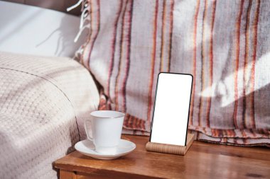 Akıllı telefon maketi, beyaz kahve fincanı ve çay tabağı, tahtadan bir sandalyede. .
