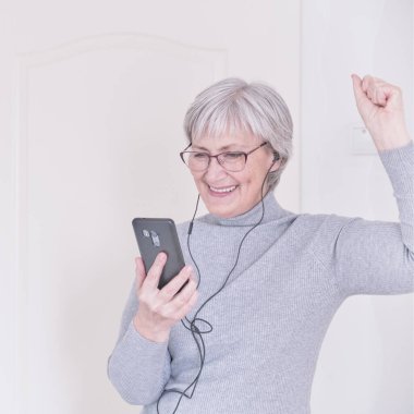 Gri saçlı, son sınıf öğrencisi bir kadın akıllı telefona bakıyor ve eğleniyor. Yaşam tarzı anı.