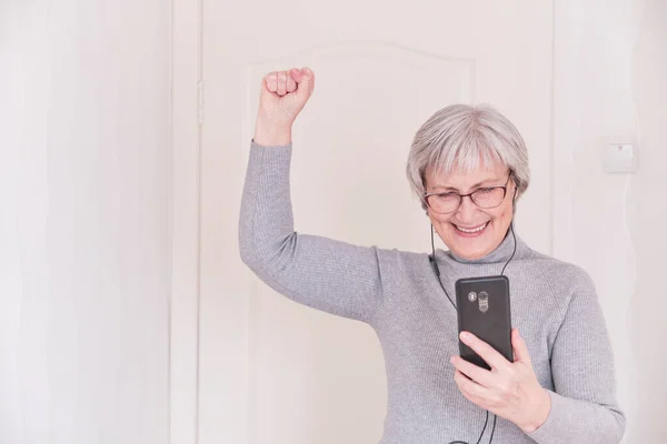 Šedovlasá starší žena, dívající se na smartphone a radující se. Okamžik životního stylu. — Stock fotografie