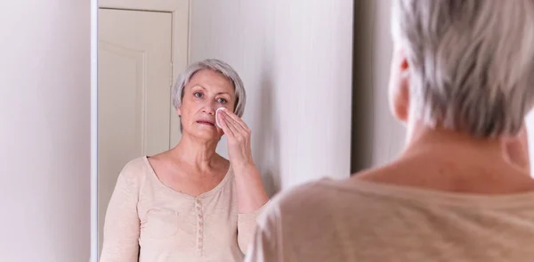 Una anciana caucásica con pelo gris corto en ropa casual cuida la piel de la cara. — Foto de Stock