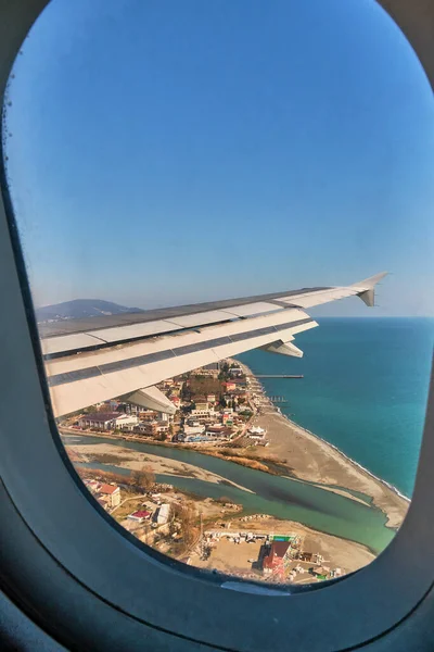 Şehrin, denizin ve nehrin üzerinde uçan bir uçağın kanadı. Soçi, Rusya