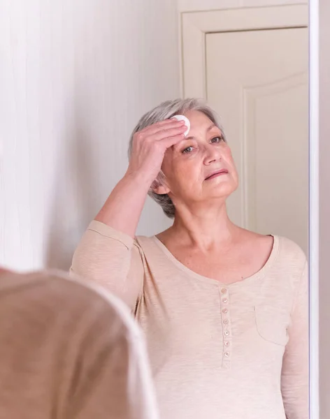 A elderly Caucasian women with short gray hair in casual clothes cares for the skin of the face. — Stock Photo, Image