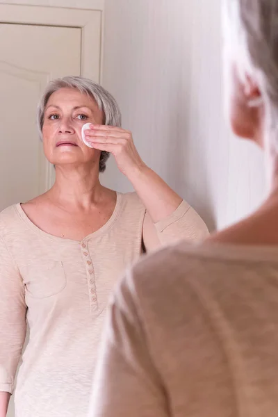A elderly Caucasian women with short gray hair in casual clothes cares for the skin of the face. — Stock Photo, Image