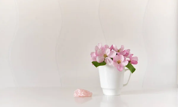 Pink mineral, pink apple tree flowers in a white coffee cup on a white coffee table