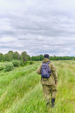 Sivrisinek kostümlü, sırt çantalı, çayırda yürüyüş yapan aktif bir adam..