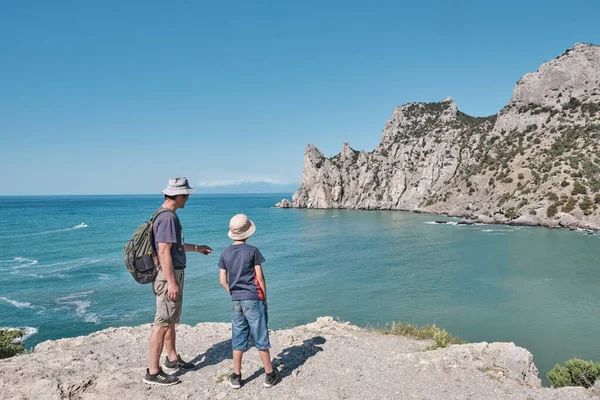 A boy and his grandfather standing on the shore of the bay and looking at the rock. — Stock Photo, Image