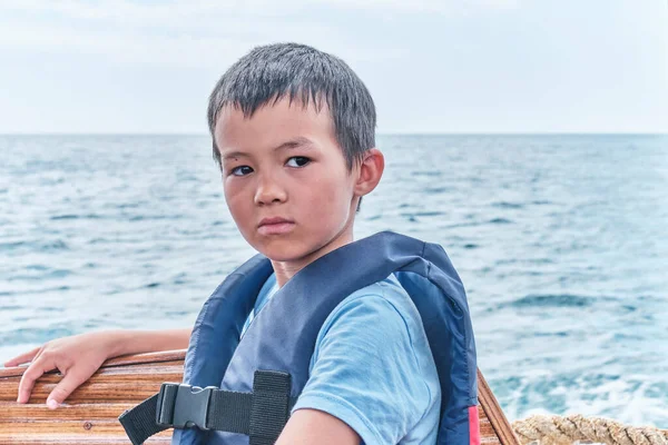 Poważny azjatycki chłopiec w kamizelce ratunkowej pływające na łodzi przyjemności na morzu. — Zdjęcie stockowe