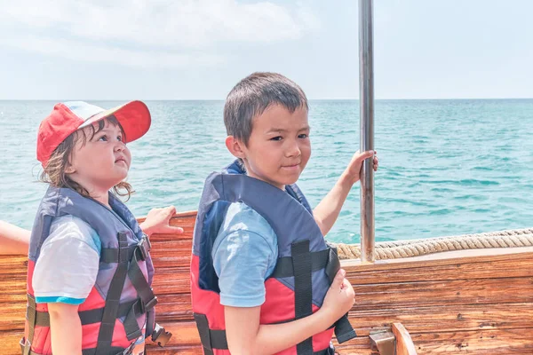 Una niña asiática y un niño, su hermano, ambos en chalecos salvavidas viaje en barco de recreo en el mar. — Foto de Stock