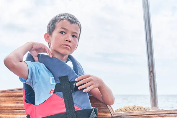 Asiático chico poniendo en chaleco salvavidas en placer mar barco. — Foto de Stock