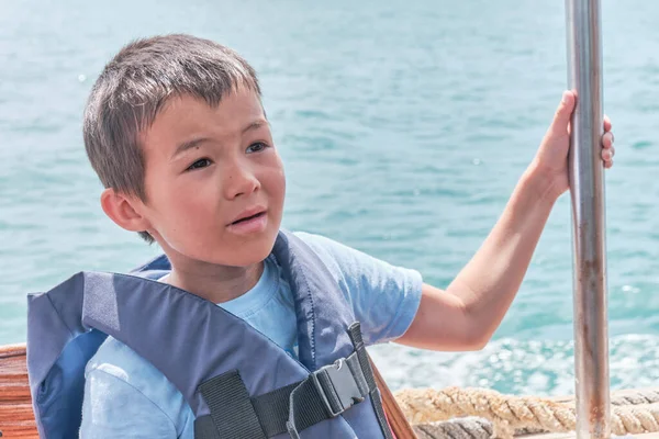 Surprised Asian boy in life jacket on pleasure boat on the sea — Zdjęcie stockowe