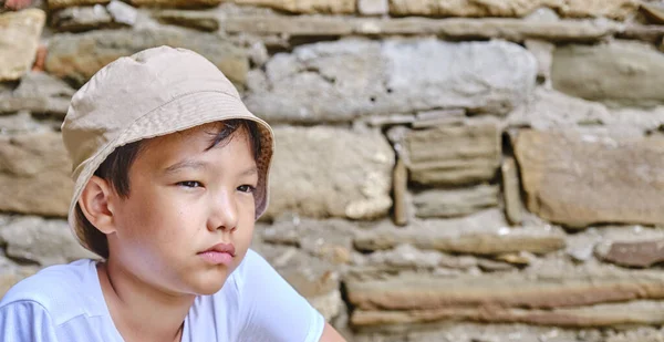Portret uroczego azjatyckiego chłopca w białej koszulce i kapeluszu panamy na tle kamiennej starożytnej ściany. — Zdjęcie stockowe