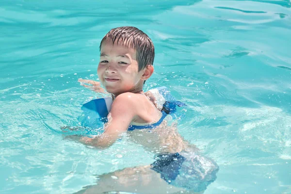 Pequeno menino asiático está aprendendo a nadar na piscina exterior — Fotografia de Stock