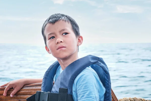 Poważny azjatycki chłopiec w kamizelce ratunkowej na łodzi rekreacyjnej na morzu. — Zdjęcie stockowe